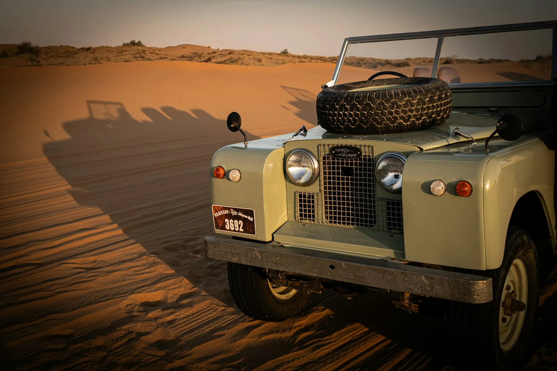 A vintage Land Rover on a sand dune in warm evening light
