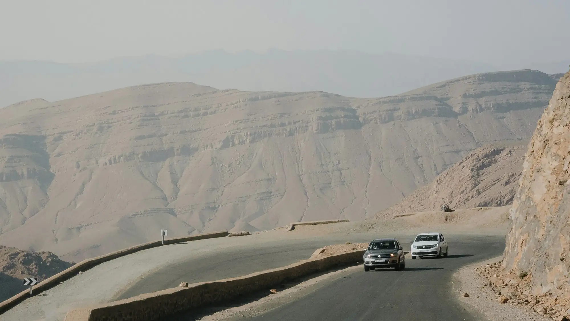 Two cars on a winding road through hazy desert mountains